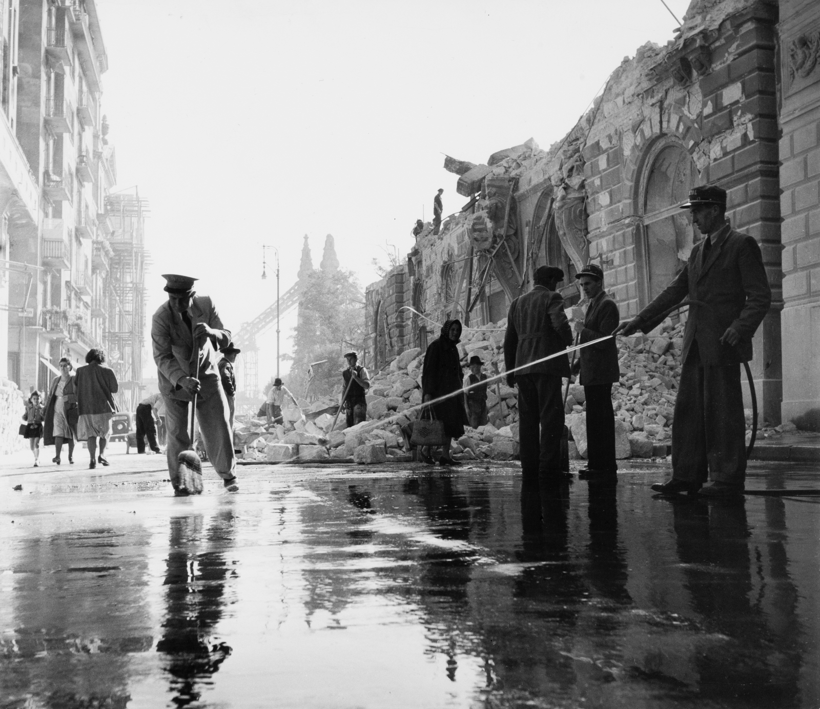 [Söprögető, a Bristol Szálló sapkáját viselő férfiak a romos Dunakorzón, Budapest], 1948, Robert Capa, Courtesy International Center of Photography | [Men wearing Bristol Hotel caps, sweeping the sidewalk on the ruined Danube Promenade, Budapest], 1948, Robert Capa, Courtesy International Center of Photography
